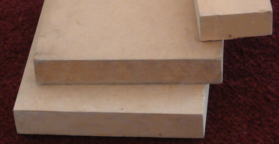 Ba tấm MDF trần màu nâu nhạt xếp chồng lệch nhau trên thảm đỏ sẫm. Cạnh cắt của từng tấm phẳng, liền một màu từ mặt trên xuống mặt dưới, không thấy lớp hay lỗ rỗng.