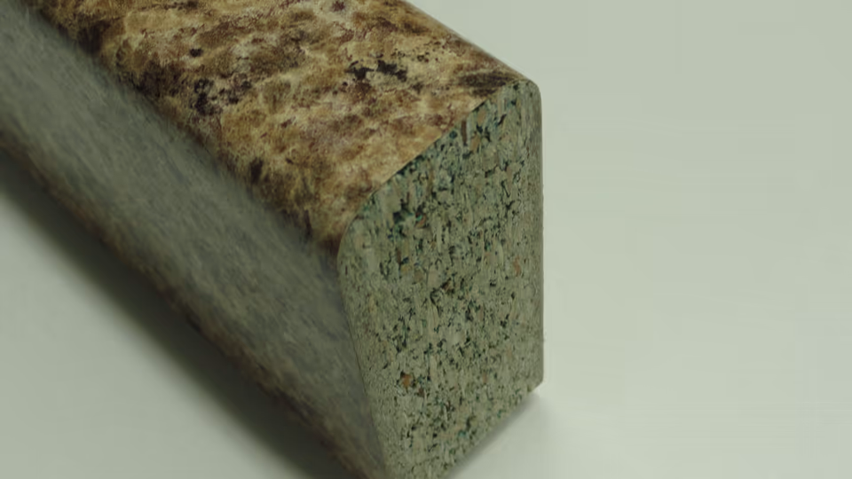 Đoạn thanh ván dăm màu xanh xám có mặt phủ laminate vân đá nâu. Lớp laminate cong liền từ mặt trên xuống một cạnh bo tròn, còn mặt cắt ngang của cốt ván dăm lộ ra ở đầu thanh.