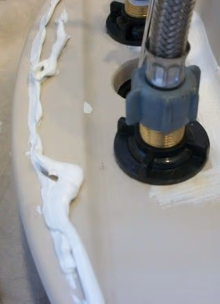 Một chậu rửa mặt lật ngửa mặt dưới lên, dọc vành chậu là một đường silicone trắng vừa bơm, bên cạnh là hai chân vòi bằng đồng có ống cấp nước inox.